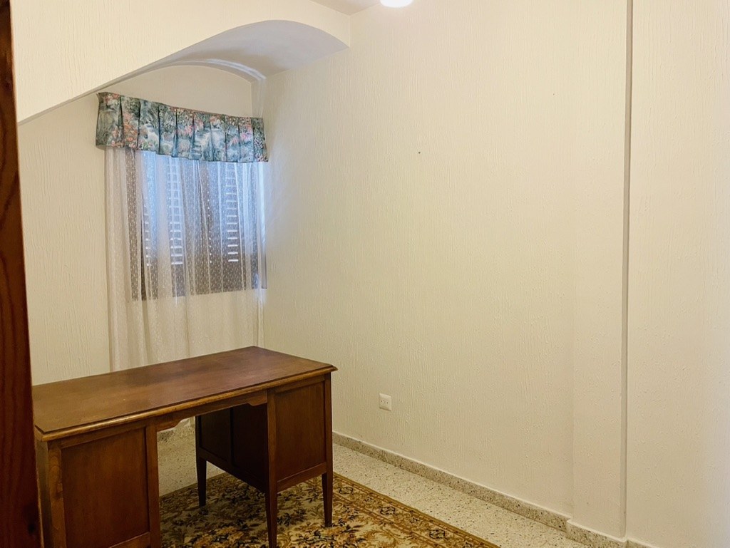 Antes: despacho con mesa de madera adelantada, alfombra estampada y visillo con cenefa en la ventana