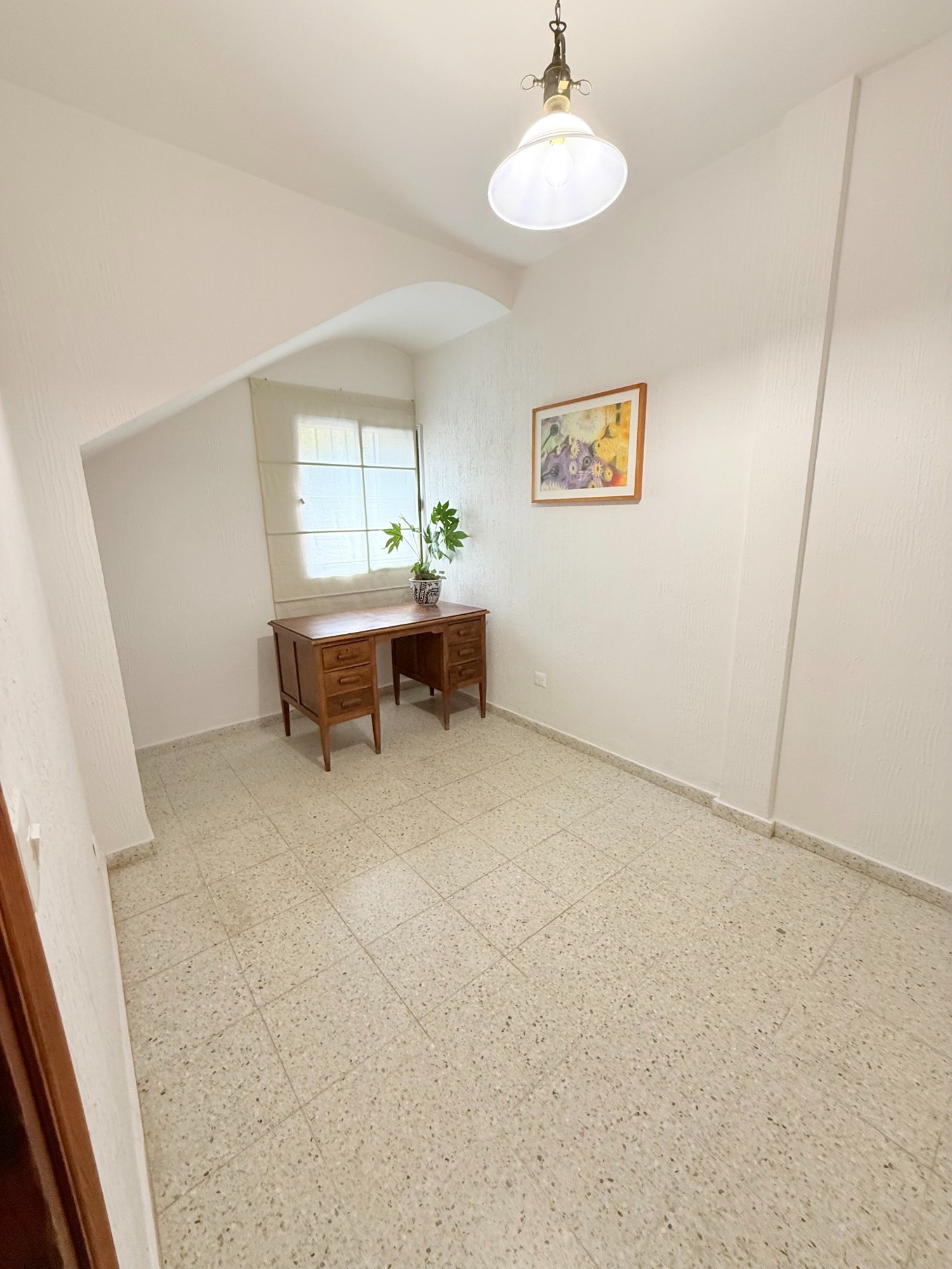 Después: mesa junto a la ventana con estor claro, planta y cuadro en la pared, con el centro de la estancia despejado