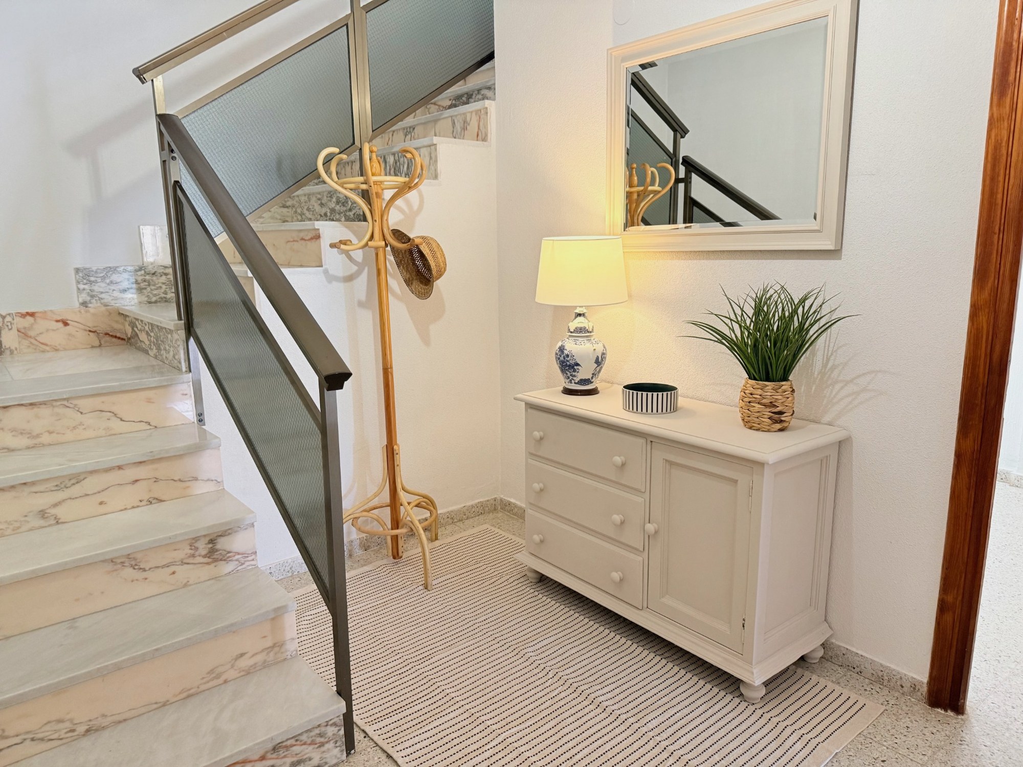 Después: mueble claro con lámpara, planta y espejo, junto a un perchero y una alfombra de rayas